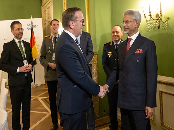 Boris Pistorius shaking hands with India's External Affairs Minister S. Jaishankar in a green-walled room at the Munich Security Conference, with officers looking on